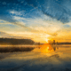 Golden sunrise reflected on a calm lake surrounded by pine trees, showcasing peaceful scenery in Yellowstone National Park.